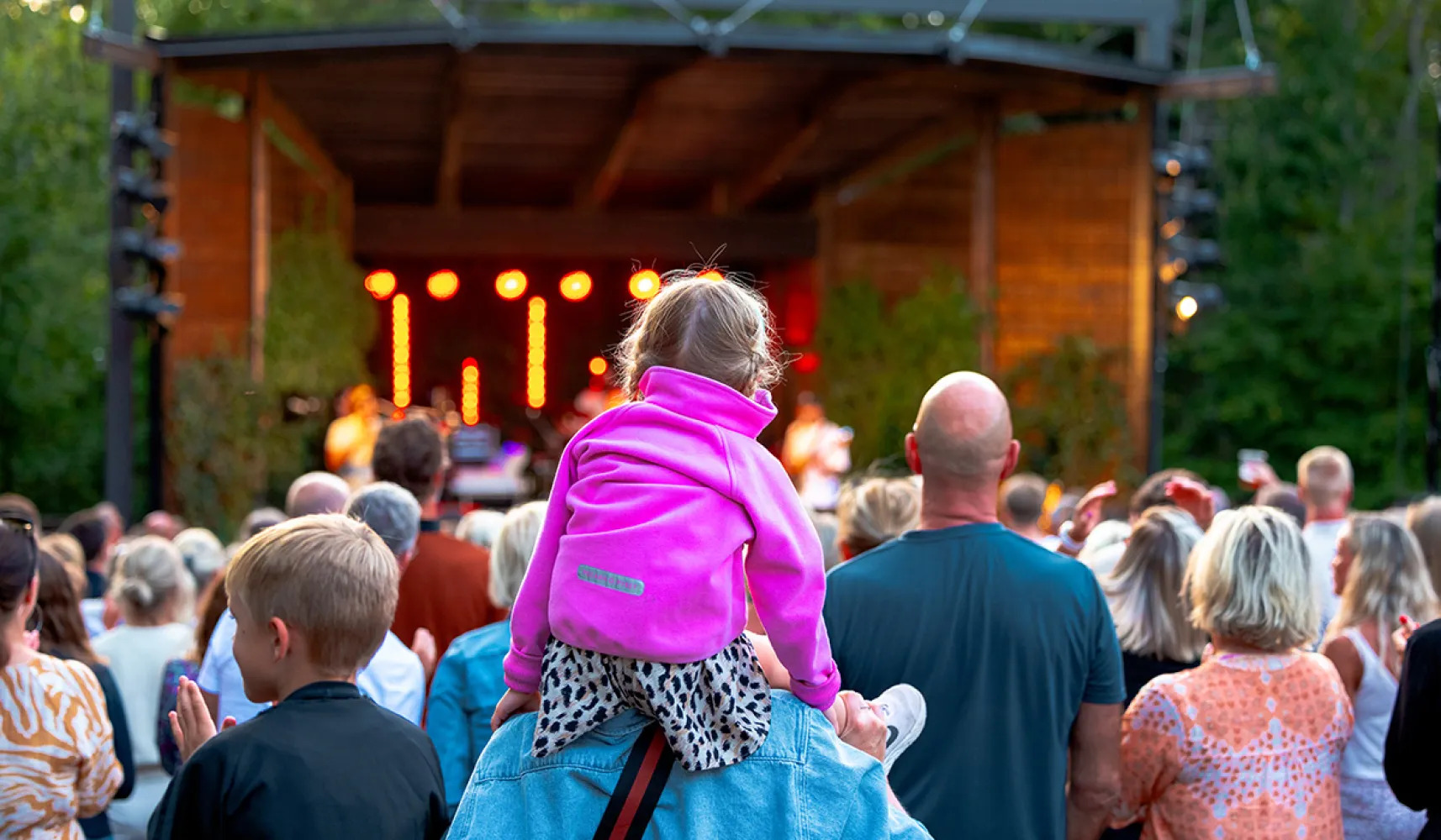 Liten flicka sitter på pappas axlar och kollar på konsert